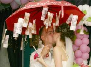 Поцелуй молодоженов под красным зонтиком с подвешенными купюрами