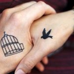 Руки с татуировкой клетки и птички